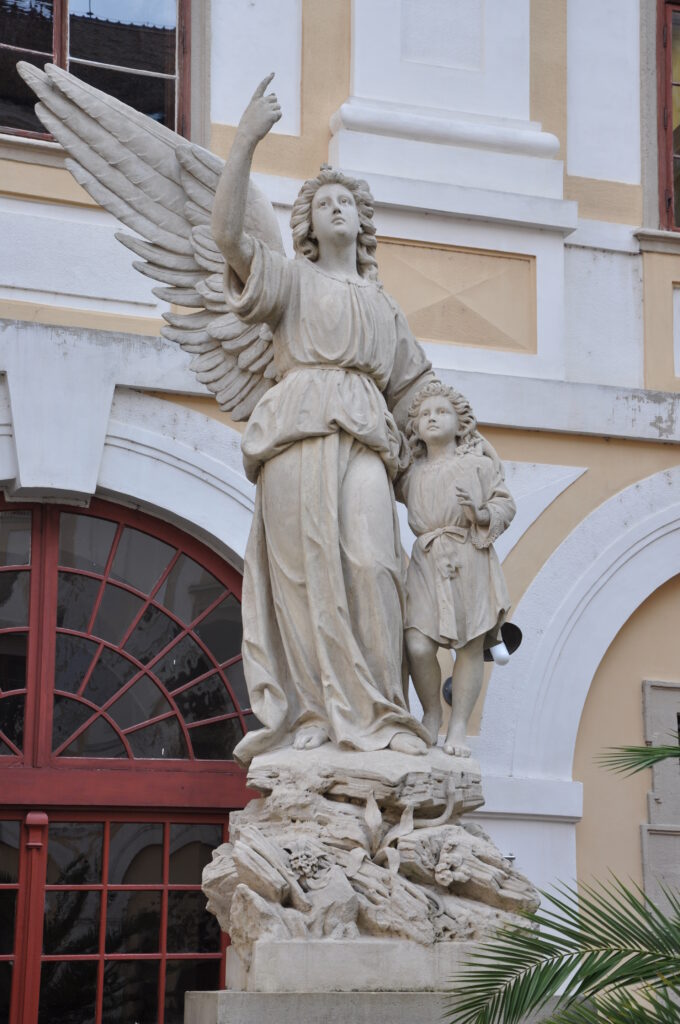 Stone statue of a winged guardian angel holding a sword that rests on the ground.