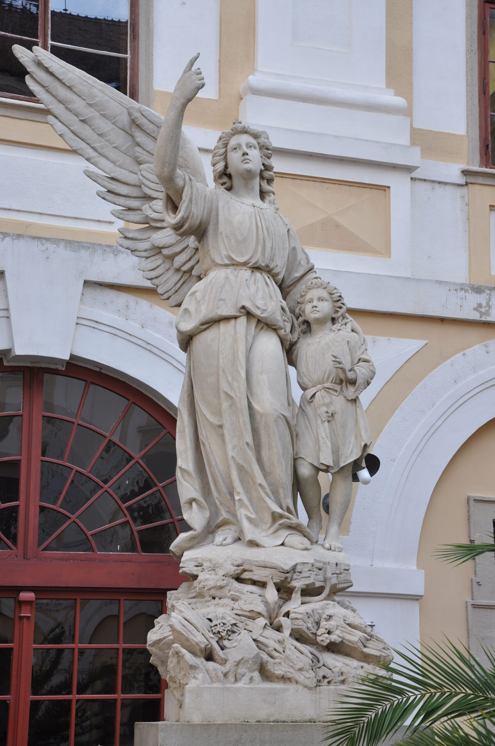 Stone statue of a winged guardian angel holding a sword that rests on the ground.