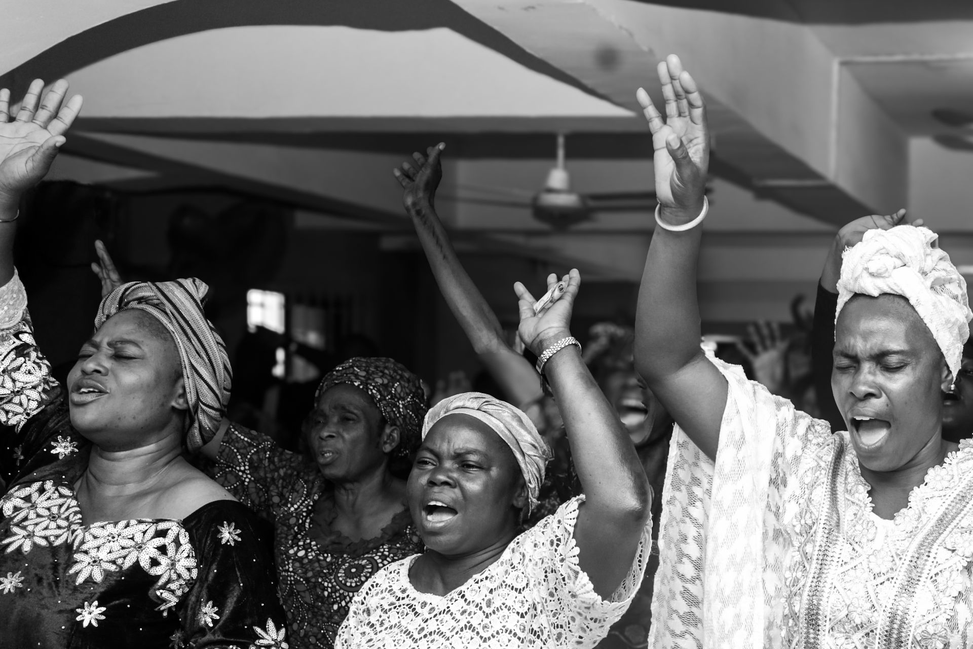 Nigerian women raising their hands in joyful worship during an indoor gathering in Lagos.