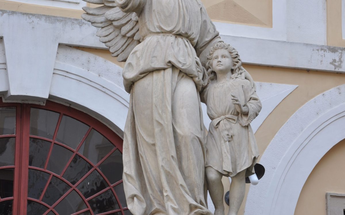 Stone statue of a winged guardian angel holding a sword that rests on the ground.