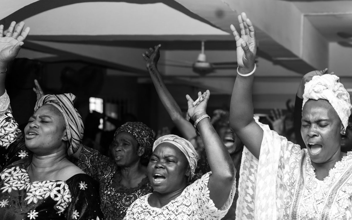 Nigerian women raising their hands in joyful worship during an indoor gathering in Lagos.